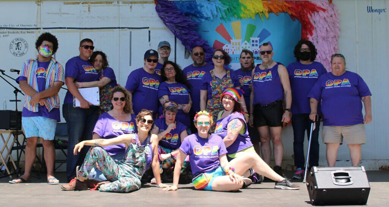 OPA organizers standing together on stage in front of rainbow colored flowers